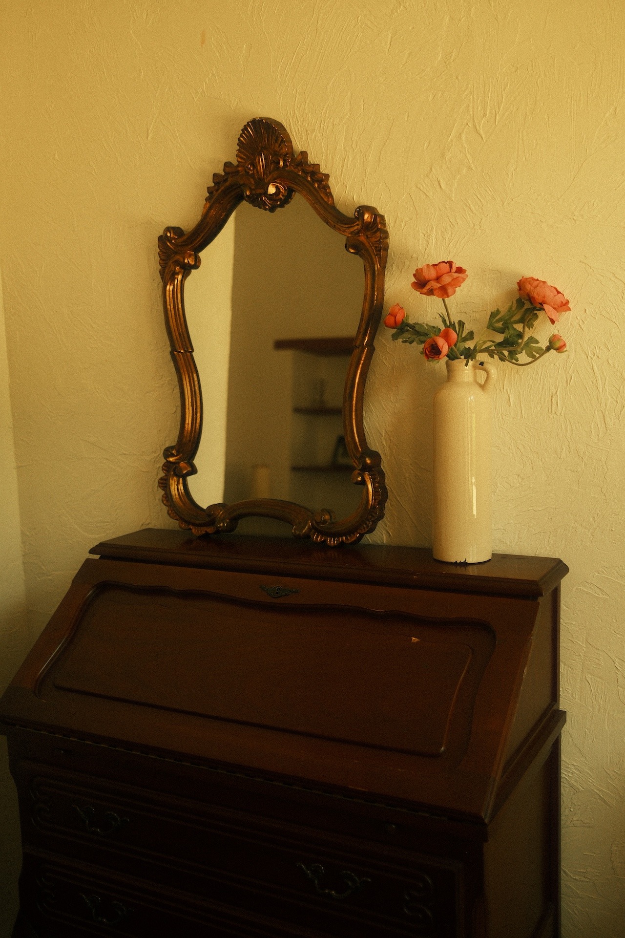 Gilded mirror and fresh flowers on a dresser in a rustic room