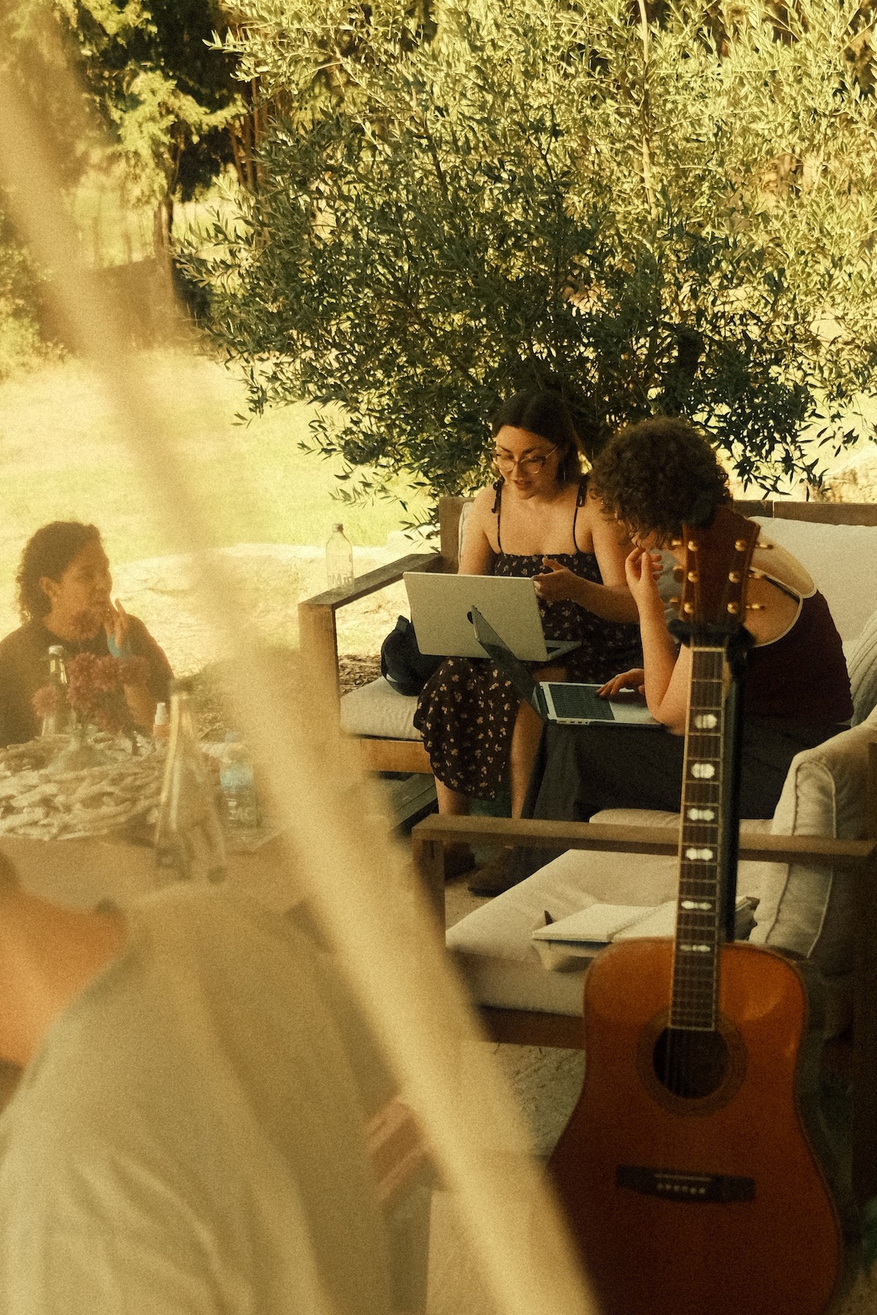 Two songwriters writing outdoors with a guitar and laptops in the sun